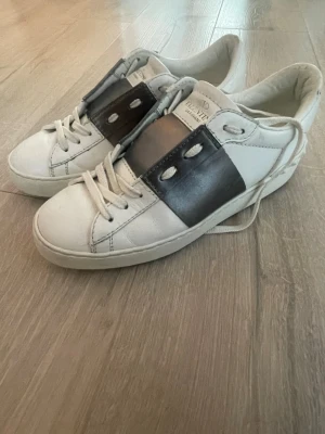 Valentino Garavani vita sneakers - Säljer ett par vita Valentino Garavani sneakers med bred silverfärgad detalj över snörningen. Skorna har klassisk rund tå, vita snören och en chunky sula. Storlek 36 men sitter som 37 (har man 36 normalt sett går det också bra att lägga in en extra sula om man vill)z skriv för fler bilder❤️