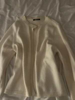 Krämvit kofta från Gina Tricot - Mysig krämvit stickad kofta från Gina Tricot med rund halsringning och ribbade kanter. Koftan har en enkel knapp upptill och är långärmad, perfekt att slänga över en t-shirt eller topp.