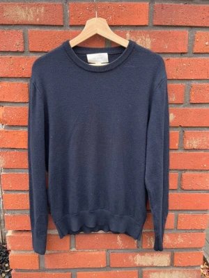 Mörkblå merino ull tröja  - En stilren mörkblå stickad tröja från Arket med rund halsringning och ribbade muddar vid ärmslut och nederkant. Perfekt basplagg i garderoben, enkel att matcha och har en klassisk passform. Materialet känns mjukt och bekvämt. Det är 100% Marino ull. Storleken är M men passar både S och M skulle jag säga. 