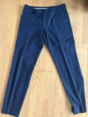 Mörkblå kostymbyxor Oscar Jacobson - Snygga mörkblå kostymbyxor från Oscar Jacobson, tillverkade i exklusivt tyg från Vitale Barberis Canonico. Ny pris 1800kr ca, knappt använd, dock två små hål på framsidan(se bild 4) men syns knappt. 