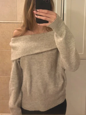 Beige off shoulder stickad tröja - Säljer en beige stickad tröja med bred off shoulder-ringning och långa ärmar. Tröjan har en oversized passform och ribbstickade muddar. Perfekt för dig som gillar en avslappnad och trendig stil🥰