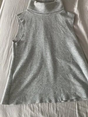 Grå polotopp från Zara - Säljer en stilren grå polotopp från Zara. Toppen är ärmlös och har en hög polokrage. Materialet är ribbat och känns mjukt mot huden, perfekt för lager på lager eller som den är. Enkel att matcha till olika outfits!