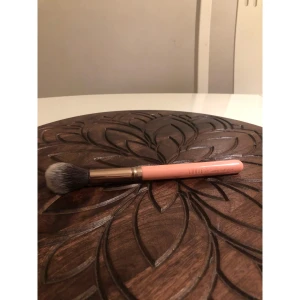 Luxie 522 Tapered Highlighter borste - Superfin sminkborste från Luxie, modell 522 Tapered Highlighter. Handtaget är persikofärgat med metallisk guld-detalj och borsten är mjuk med vit och svart syntetisk borst. Perfekt för att applicera highlighter med precision.