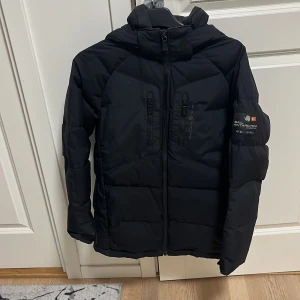Svart Sail Racing pufferjacka med huva - Säljer en svart vinter jacka från sail racing. Jackan är i bra skick, Storlek Xs - 160 med oranga detaljer på vänster arm med sail racing märket, jackan är köpt hos sail racing för 3000 och säljer den för 1250 vilket är ett rejält bra pris för en sån här jacka i den här konditionen som den är i.