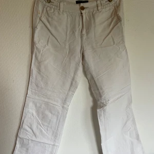 Beiga linnebyxor från Banana Republic - Snygga beiga linnebyxor från Banana Republic med raka ben och klassisk passform. Byxorna har fickor fram, bälteshällor och stängs med knapp och dragkedja. Perfekta för en avslappnad och stilren look.