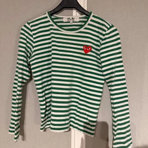 Randig långärmad tröja Comme des Garçons - Säljer en grön och vit randig långärmad tröja från Comme des Garçons Play. Fin tröja men tyvärr en liten defekt vid lappen i nacken, men det ör ytterst litet och syns knappast.