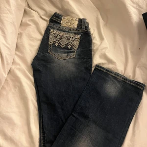 Miss Me jeans med broderad ficka - Snygga mörkblå jeans från Miss Me med broderade detaljer och pärlor på bakfickan. Modellen är midwaist och bootcut, med slitningar och kontrastsömmar. Perfekta för dig som vill sticka ut med coola detaljer och unik look.