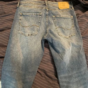 Jack & Jones Tapered Mike jeans blå - Snygga blå jeans från Jack & Jones, modell Tapered Mike. Klassisk femficksdesign med gul kontrastsöm och läderpatch bak. Jeansen har en tapered passform som ger en modern siluett och är tillverkade i slitstarkt denimtyg.