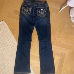 Mörkblå bootcut jeans med kontrastsömmar - Snygga mörkblå jeans med bootcut passform och markerade kontrastsömmar. Bakfickorna har dekorativa sömmar och knappar. Jeansen har klassisk femficksdesign och stängs med dubbla knappar framtill. Perfekta för dig som gillar en tidlös look.