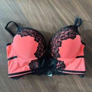 Korallfärgad spetskorsett med svarta detaljer - Snygg korsettopp i korall med svarta spetsdetaljer och vadderade kupor. Axelbanden är justerbara och spetsen ger en extra touch. Perfekt för att lyfta din outfit med en färgstark och feminin look. Endast provad! Säljes då den tyvärr var för stor för mig. 🌸💞