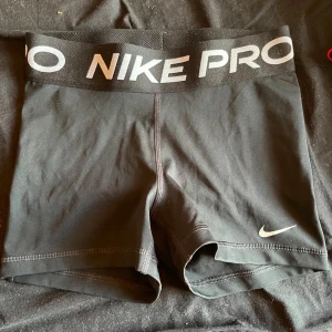 Svarta Nike Pro träningsshorts - Svarta Nike Pro shorts med bred elastisk midja och vit logga framtill. Snygg, tight passform som sitter skönt vid träning. Materialet är stretchigt och andas, perfekt för gymmet eller sport. Klassisk stil med diskret Nike Swoosh på benet. Oanvända, men utan prislapp kvar.