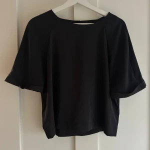 Svart blus från Bik Bok - En svart, stilren blus från Bik Bok i storlek M. Blusen har korta, vida ärmar och rund halsringning. Tillverkad i ett mjukt och lätt material som ger ett snyggt fall. Perfekt att matcha med både jeans och kjol.