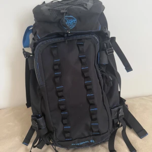 Svart och blå Integral 45 ryggsäck - Stor och robust ryggsäck från NCC Integral, modell 45L. Svart med blå detaljer och broderad logga på locket. Flera justerbara remmar, vadderad rygg och höftbälte för extra komfort. Perfekt för längre äventyr och packning. Snygga blå sömmar och smarta fästen framtill.