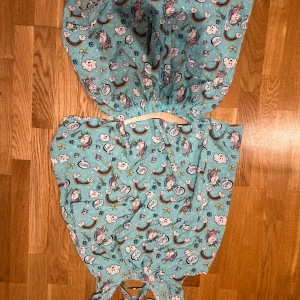 Turkos Pyamas set med enhörningar - Söt turkos Pyamas set med gulligt enhörningsmönster, regnbågar och moln. Klänningen har snörning i ryggen och är tillverkad i mjuk bomull. Perfekt för dig som gillar färgglada och lekfulla prints.