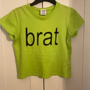 Neongrön Charli XCX t-shirt från Bershka - Neongrön t-shirt från Charli XCX x Bershka med svart 'brat'-print på framsidan, Klassisk rund hals och korta ärmar. Köpt på Vinted och jag har använt den en gång⭐️ Inga fläckar eller liknande 