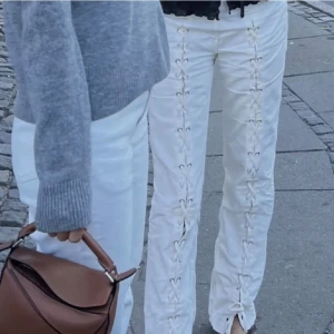 Vita byxor med snörningsdetaljer -  byxor med snörning längs hela framsidan av benen. Byxorna har rak passform 