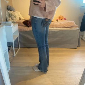 Blå bootcut jeans från Wrangler - Säljer ett par klassiska blå bootcut jeans från Wrangler med snyggt slitna detaljer och hål på ena knät. Jeansen har låg midja, fem fickor och ikonisk W-söm på bakfickorna. Perfekta för dig som gillar en avslappnad och trendig look❤️Passar S-M🌸