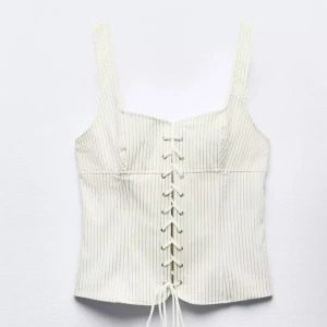 Vit randig korsett med snörning💕 - Säljer en vit korsett med tunna svarta ränder och snygg snörning framtill. Toppen har breda axelband och är figurnära med en croppad passform. Sparsamt använd ❤️