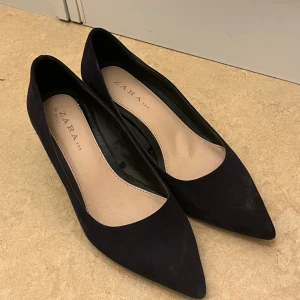 Svarta mockapumps från Zara - Snygga svarta pumps från Zara i mocka med spetsig tå och stabil, låg klack. Perfekta för dig som vill ha en klassisk och stilren sko med lite edge. Skorna har en mjuk innersula i beige och en chunky klack som ger extra komfort.