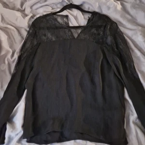 Svart blus med spets från Zara Woman - Säljer en svart blus från Zara Woman i storlek L. Blusen har långa ärmar och snygga spetsdetaljer upptill och på axlarna, samt v-ringad hals. Materialet är lätt och ger en elegant känsla. Perfekt för dig som gillar stilrena och trendiga plagg.