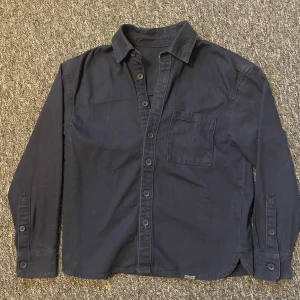 Mörkblå overshirt från KIABI XXS - Snygg mörkblå overshirt från KIABI i storlek XXS. Skjortan har klassisk krage, knappstängning framtill. Perfekt för dig som gillar enkel och stilren look.
