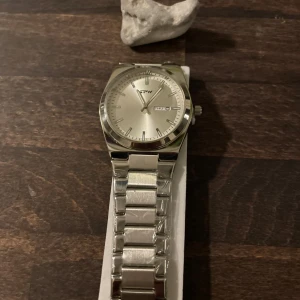 Silverfärgad klocka från TPW - Stilren klocka från TPW i helsilver med klassisk länkarmband och rund urtavla. Urtavlan är silverfärgad med tydliga index och dag/datumvisning. Klockan har en modern och minimalistisk look som passar till många stilar. Perfekt som fars dag present eller julklapp. Kom gärna med prisförslag 