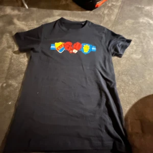 Svart t-shirt med boxningsmotiv - Svart t-shirt med tryck av boxningshandskar och klubbmärken i rött, blått och gult på bröstet. Klassisk passform från DIF boxning