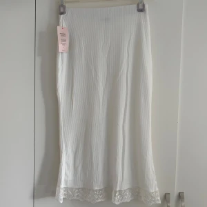 Vit långkjol med spets från Nelly - Alldeles NY med fortfarande lapp kvar vit kjol från Nelly. Har såetskanted blommor nedantill. Säljs inte längre på hemsidan. Skriv om du har frågor🌸💗