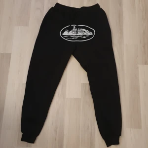 Svarta mjukisbyxor med tryck - Svarta mjukisbyxor med resår och snörning i midjan samt ett stort vitt tryck framtill. Byxorna har muddar vid bensluten och är tillverkade i mjukt material, perfekta för chill eller träning.