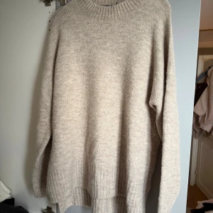 Beige stickad tröja från Vero Moda - Mysig beige stickad tröja från Vero Moda med rund halsringning och ribbade muddar. Tröjan har en loose passform och långa ärmar, perfekt för lager-på-lager under kyliga dagar.