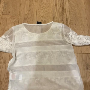 Vit spetsblus från Vila, storlek L - Säljer en vit blus från Vila i storlek L. Blusen har halvtransparent tyg med breda spetsränder och blommiga detaljer. Rund halsringning och korta ärmar med vacker spets. Perfekt för dig som gillar romantisk och feminin stil. Skulle säga att tröjan även passar s och m