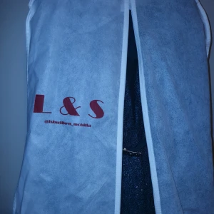 Turkos långklänning med bälte från Arnida - Säljer en turkos långklänning från Arnida med glittriga detaljer och textur i tyget. Klänningen har långärmade spetsärmar, v-ringning och ett snyggt bälte med dekorerat spänne. Dragkedja i ryggen och svepande kjol för extra drama.