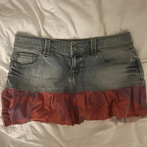 Lågmidjad jeanskjol - Säljer en lågmidjad, kort jeanskjol med tygdetalj. Jag har klippt av den själv så kanske inte helt rakt, men det går enkelt att fixa. Jättefint skick annars!