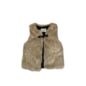 Beige pälsväst från Zara Girls - Supermjuk beige pälsväst från Zara Girls med snyggt spänne framtill. Västen har en fluffig känsla och är fodrad med svart tyg på insidan. Perfekt för att lyfta vilken outfit som helst med lite extra stil.
