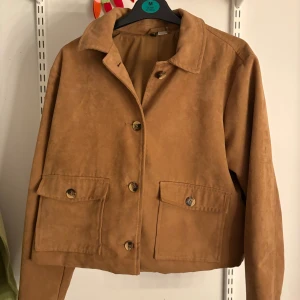 Mockajacka från H&M - Snygg mockajacka från H&M i varm brun färg. Jackan har klassisk krage, stora fickor med knappar framtill och stängs med knappar. Croppad passform och långärmad, därför köpte jag den i L så att den sitter större och längre på!🌸