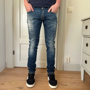 Replay Anbass jeans blå - Säljer ett par Replay Anbass jeans i blå tvätt med snyggt slitna detaljer och klassiska bakfickor. Jeansen har smal passform och sitter tight längs benen. Materialet är stretchigt denim som ger en bekväm känsla hela dagen.