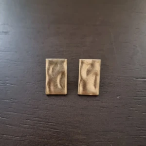 Rektangulära guldiga örhängen - Snygga rektangulära örhängen i guldton med vågig, matt yta som ger en cool och modern vibe. Perfekta för dig som gillar minimalistisk design med en twist. 