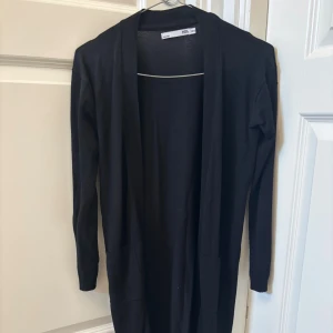 Svart lång cardigan från lager 157 - Lång svart kofta från lager 157 i enkel och stilren design. Koftan har öppen front, långa ärmar och två fickor framtill. Använd endast ett fåtal gånger!💕