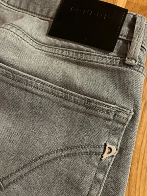 Grå DonDup jeans Slim Fit - Snygga grå jeans från DonDup med Slim passform och klassisk femficksdesign. Jeansen har en svart DonDup-logga på bakfickan och metallmärke på fickan. Materialet är mjukt denim och färgen är ljusgrå med tvättad look. Perfekt för dig som gillar stilrena och moderna jeans. Modellen Är 174 59kg