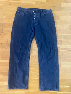 Weekday Space Relaxed Straight Jeans - Säljer ett par svarta Weekday Space Relaxed Straight Jeans med klassisk femficksdesign och knappgylf. Jeansen har rak passform och avslappnad stil, tillverkade i jeansmaterial. Perfekta för dig som gillar en chill och enkel look. Storlek 32/32