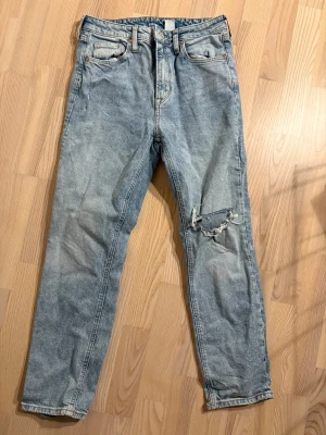 Vintage slim high waist jeans - Snygga ljusblå jeans med slim fit och hög midja. Klassisk femficksmodell i denim med slitning och hål på ena benet för en cool, avslappnad vibe. Perfekt för dig som gillar retrostil och vill sticka ut med detaljer.
