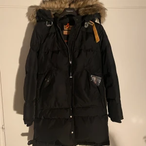 Svart Parajumpers dunjacka med päls - Skick: 10/10 (använd endast fåtal gånger, ca 5 ), Nypris: runt 8 tusen, Modell: Masterpiece series, Självklart äkta! Luvan går att ta av om man vill! Svart dunjacka från Parajumpers med päls på huvan och coola detaljer som dragkedja och knappar. Jackan har lång passform, två stora fickor och snygga märkespatchar. Perfekt för kalla vinterdagar och har slim fit. Passar kvinnor! 