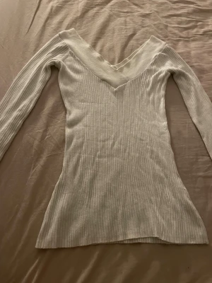 Vit ribbad långärmad topp med v-ringning - Säljer en stilren vit topp med ribbad struktur och djup v-ringad hals. Toppen har lång ärm. Materialet känns mjukt och stretchigt. Passar dig som gillar enkla men snygga plagg.
