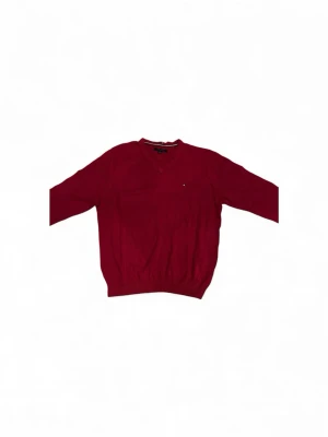 Röd stickad tröja Tommy Hilfiger XL - Snygg röd stickad tröja från Tommy Hilfiger i storlek XL. Tröjan har v-ringad hals och långärmade ärmar, med en liten logga broderad på bröstet. Perfekt för dig som gillar klassisk stil med en modern touch. En perfekt julklapp 