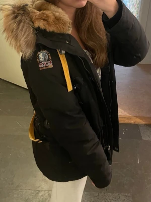 Svart Parajumpers parkajacka med päls - Säljer en svart äkta Parajumpers parkajacka Doris med fluffig päls runt huvan och snygga gula detaljer. Jackan har både dragkedja och knappar framtill, samt flera praktiska fickor. Storlek M ( jag har vanligt vis S/XS i jackor för jämförelse) Nypris: 8999 