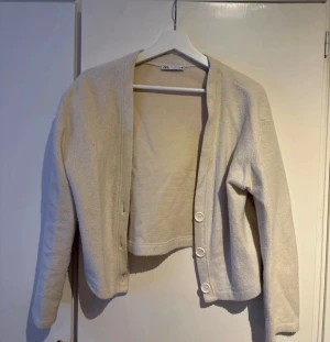 Beige kofta från Zara med knappar - Säljer en stilren beige kofta från Zara i storlek M. Koftan har lång ärm, tre stora knappar framtill och är tillverkad i ett mjukt stickat material. Köpt för något år sedan men knappt använd