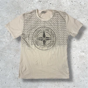 Stone Island T-Shirt - Säljer denna vita Stone Island T-Shirten med svart tryck. Tröjan kommer i stl S och är i mycket bra skick. Hör av er vid frågor, pris kan diskuteras vid snabb affär!