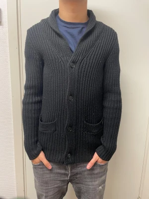 Stickad cardigan - Riktigt fet svart stickad cardigan. Bra skick. Har ett litet håll vänstra fickan (se bild 4). Modellen är 173cm, 64kg. Pris kan självklart diskuteras!!
