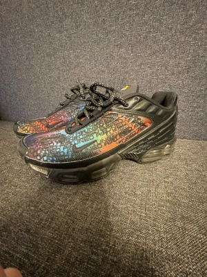 Nike Air Max Plus Tn med färgglatt mönster - Nike Air Max Plus Tn sneakers med svart bas och färgglatt gradientmönster i blått, rött och orange. Skorna har snörning, platt sula och tydliga Tn-detaljer på plösen och hälen. Materialet är syntet och mesh, med en unik grafisk design över hela ovandelen. Nypris ligger runt 2000kr