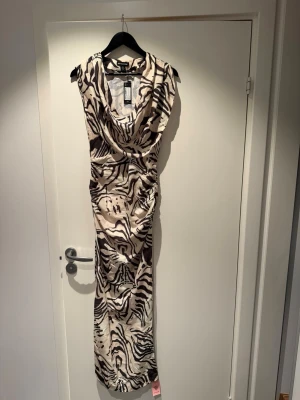 Zebramönstrad långklänning PrettyLittleThing - Säljer en snygg långklänning från PrettyLittleThing med zebramönster i svart och beige. Klänningen har draperad halsringning och är ärmlös. Har aldrig använts. Storlek 32